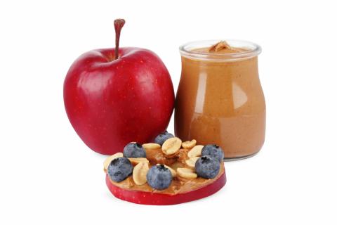 An apple next to a jar of nut butter and an apple slice with nut butter spread on it with blueberries and nuts